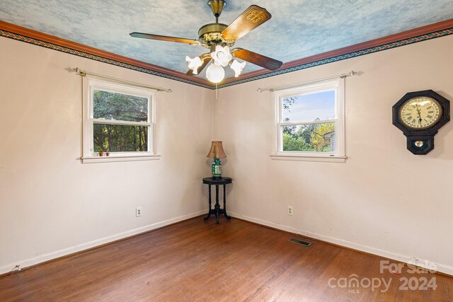 empty room with a textured ceiling, ceiling fan, ornamental molding, and hardwood / wood-style floors