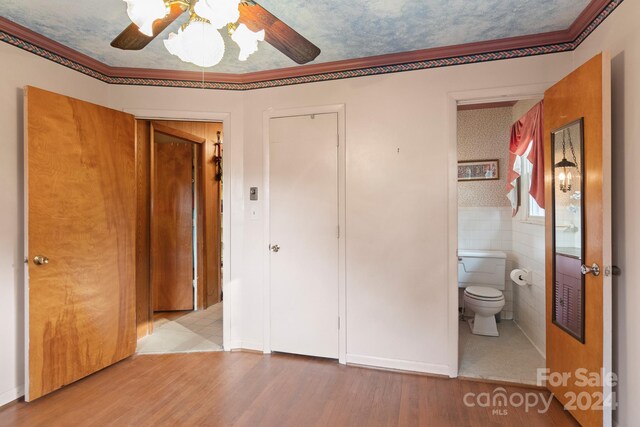 unfurnished bedroom featuring ensuite bathroom, light hardwood / wood-style flooring, tile walls, ceiling fan, and ornamental molding