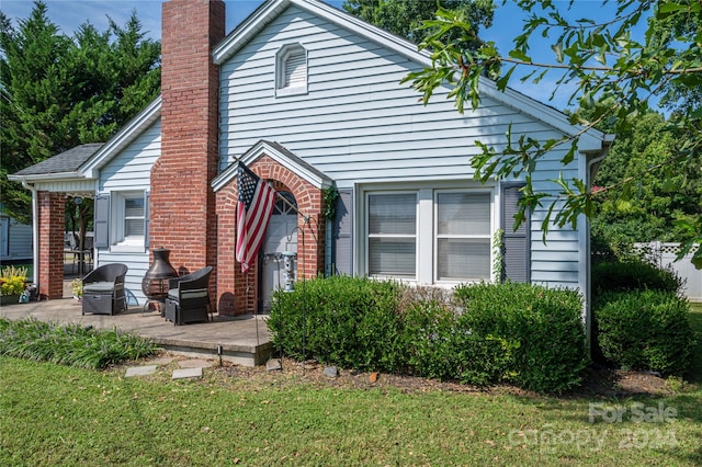 view of front of property featuring a patio area, a chimney, a front lawn, and brick siding