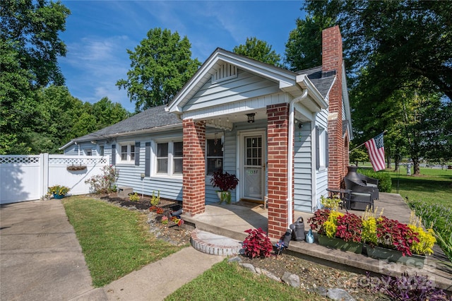 view of front facade featuring brick siding, fence, a chimney, and a front lawn