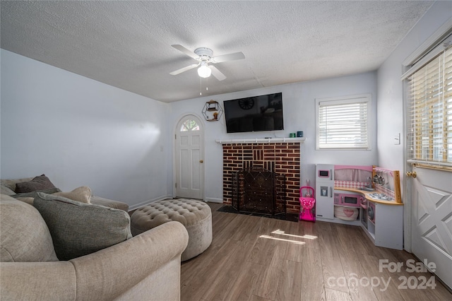 living room with hardwood / wood-style floors, ceiling fan, a brick fireplace, and a textured ceiling