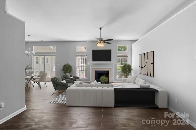 living room featuring a wealth of natural light, a tiled fireplace, ceiling fan with notable chandelier, and wood-type flooring