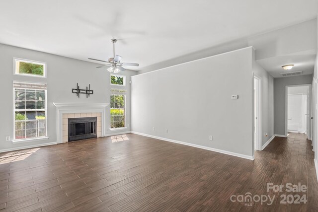 unfurnished living room with dark hardwood / wood-style flooring, a healthy amount of sunlight, a tile fireplace, and ceiling fan