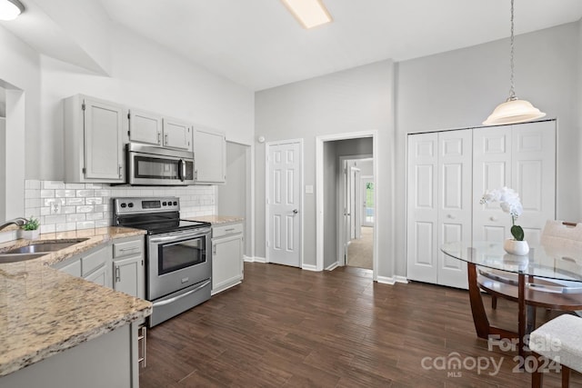 kitchen with dark hardwood / wood-style floors, hanging light fixtures, appliances with stainless steel finishes, light stone countertops, and sink