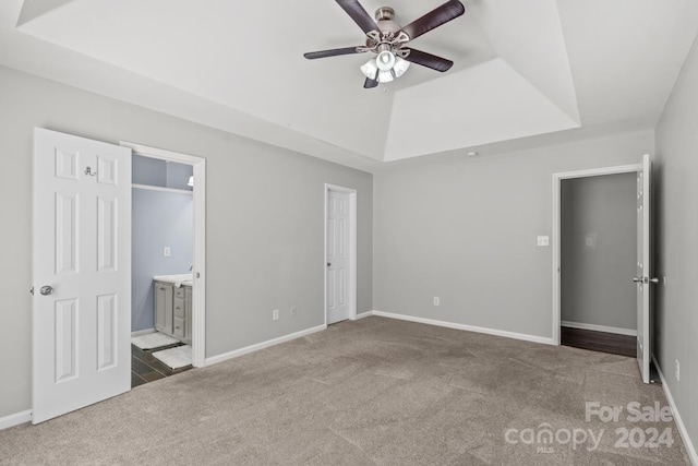 unfurnished bedroom featuring ceiling fan, a raised ceiling, carpet floors, and ensuite bath