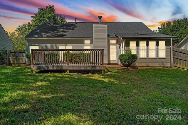 back house at dusk with a wooden deck and a yard