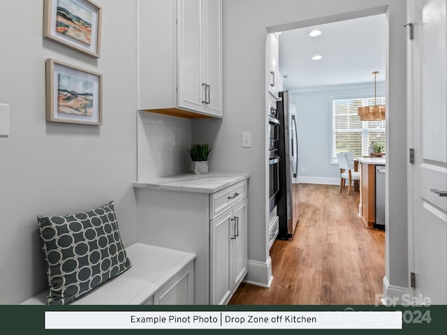 kitchen with hanging light fixtures, white cabinetry, stainless steel appliances, light hardwood / wood-style floors, and decorative backsplash