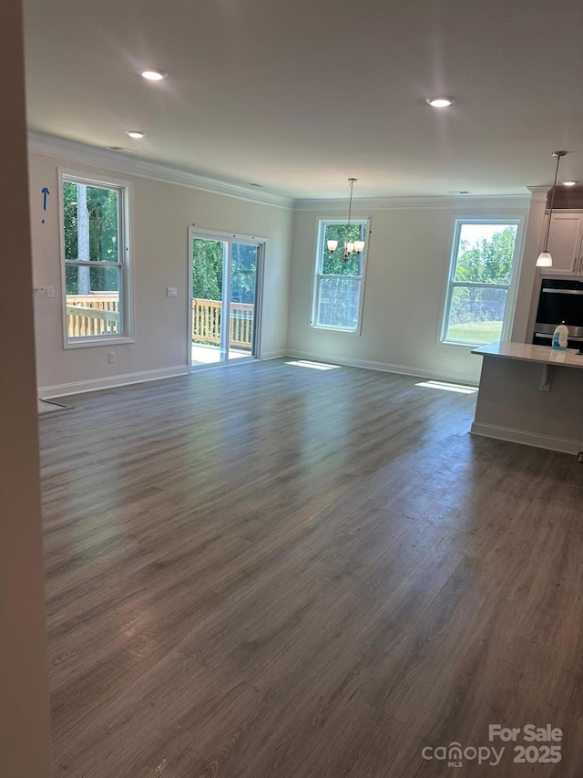 unfurnished living room with a notable chandelier, ornamental molding, dark hardwood / wood-style flooring, and a wealth of natural light