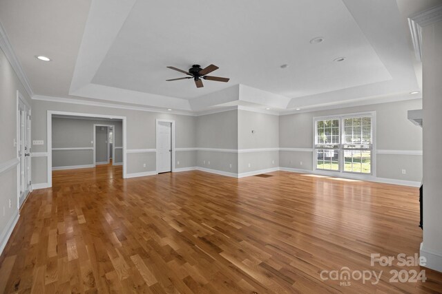 unfurnished living room featuring ornamental molding, a raised ceiling, wood-type flooring, and ceiling fan