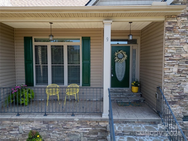 doorway to property featuring a porch, stone siding, and a shingled roof