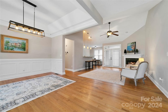 interior space with a wainscoted wall, vaulted ceiling with beams, a high end fireplace, ceiling fan, and wood finished floors