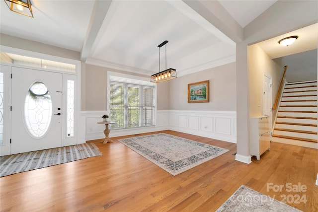 entrance foyer featuring wainscoting, stairway, beamed ceiling, light wood-type flooring, and a decorative wall