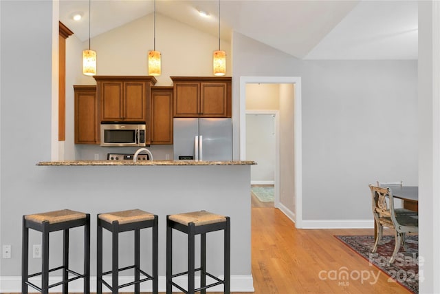 kitchen featuring light wood-style floors, appliances with stainless steel finishes, brown cabinetry, a kitchen bar, and pendant lighting