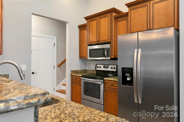 kitchen with appliances with stainless steel finishes, a sink, light stone countertops, and brown cabinets