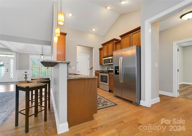 kitchen featuring light wood-style flooring, appliances with stainless steel finishes, brown cabinets, and light stone counters