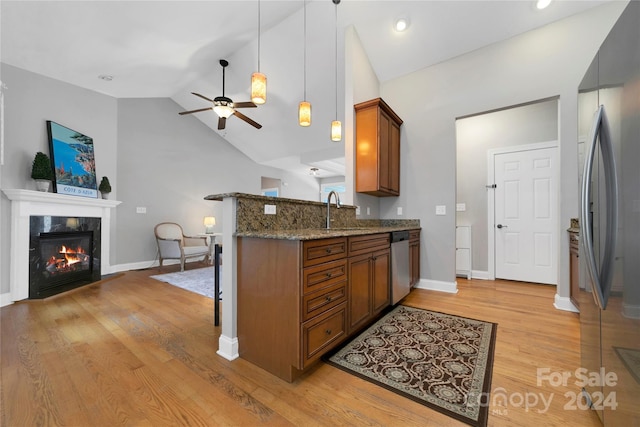 kitchen featuring stainless steel appliances, a fireplace with flush hearth, stone countertops, brown cabinetry, and a kitchen bar