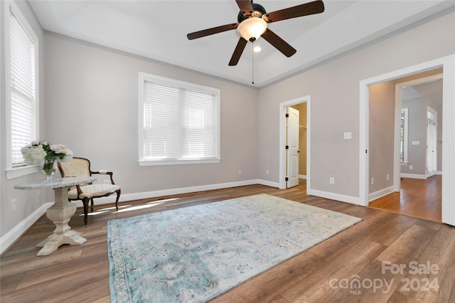 living area featuring a raised ceiling, wood finished floors, a ceiling fan, and baseboards