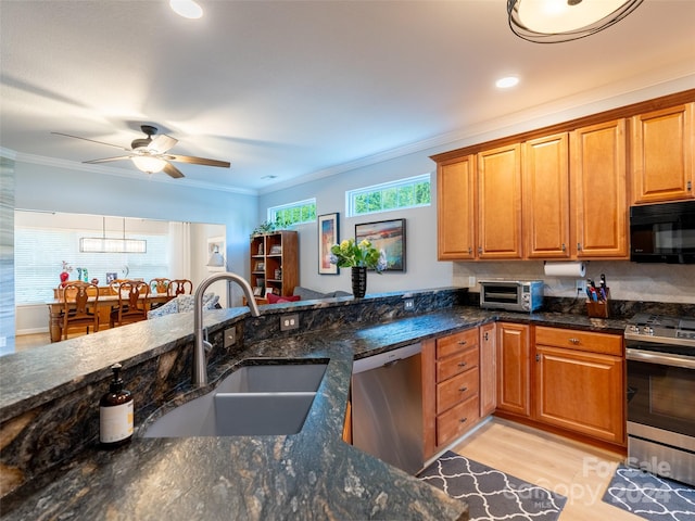 kitchen featuring stainless steel appliances, light hardwood / wood-style flooring, sink, ceiling fan, and dark stone countertops