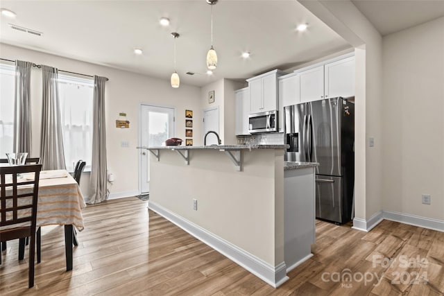 kitchen featuring appliances with stainless steel finishes, light hardwood / wood-style floors, a kitchen bar, an island with sink, and white cabinetry