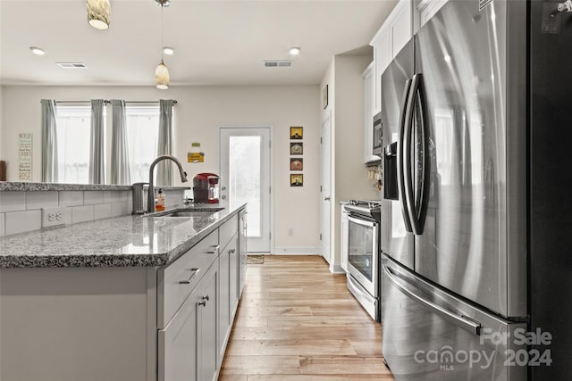 kitchen featuring stone countertops, appliances with stainless steel finishes, a kitchen island with sink, light hardwood / wood-style floors, and sink