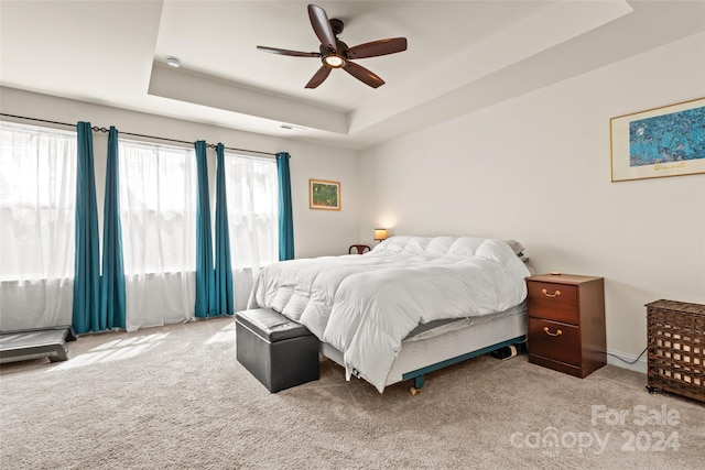 carpeted bedroom with a raised ceiling and ceiling fan