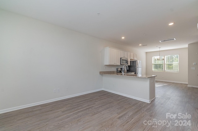 kitchen featuring a chandelier, wood-type flooring, white cabinetry, appliances with stainless steel finishes, and kitchen peninsula