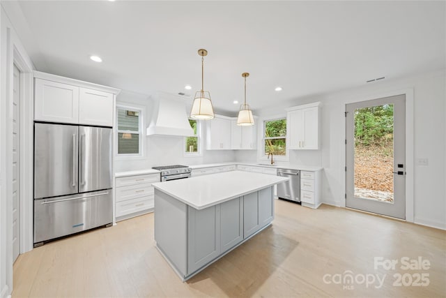 kitchen featuring white cabinetry, stainless steel appliances, decorative light fixtures, a kitchen island, and custom range hood