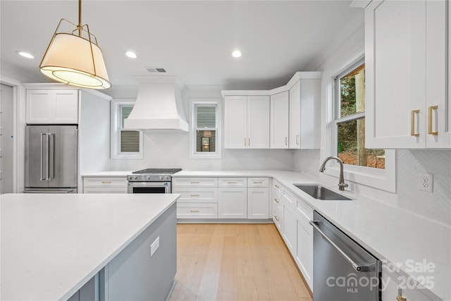 kitchen with sink, pendant lighting, high quality appliances, white cabinets, and custom range hood