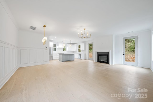 unfurnished living room with ornamental molding, light hardwood / wood-style flooring, and an inviting chandelier