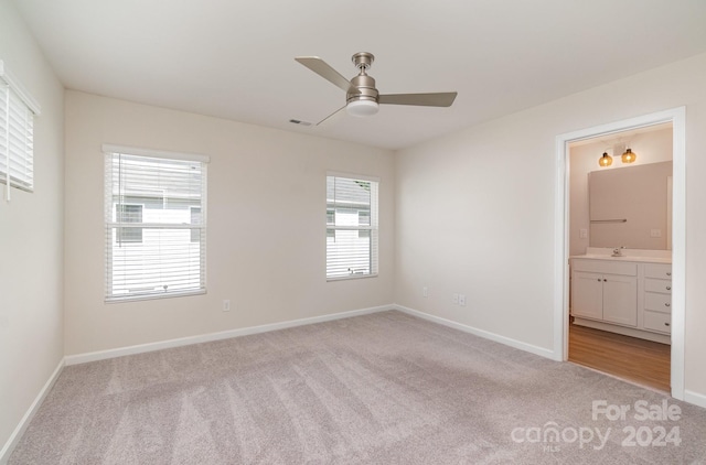 unfurnished bedroom featuring light carpet, ensuite bathroom, sink, and ceiling fan