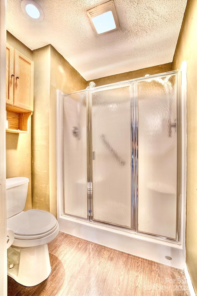 bathroom with hardwood / wood-style floors, toilet, a textured ceiling, and a shower with shower door