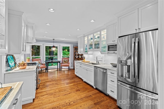 kitchen featuring light wood-type flooring, backsplash, hanging light fixtures, appliances with stainless steel finishes, and white cabinets