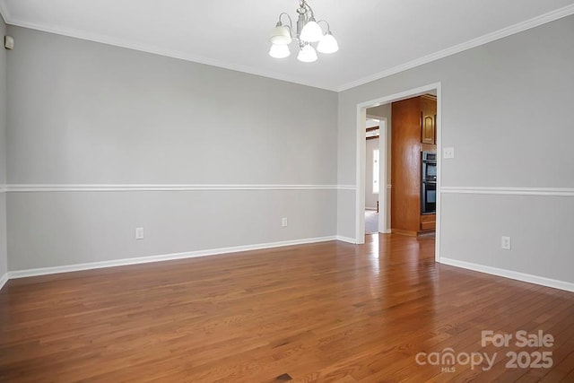 spare room featuring a chandelier, ornamental molding, baseboards, and wood finished floors