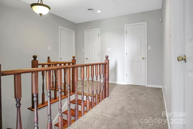 hall with carpet, visible vents, baseboards, and an upstairs landing