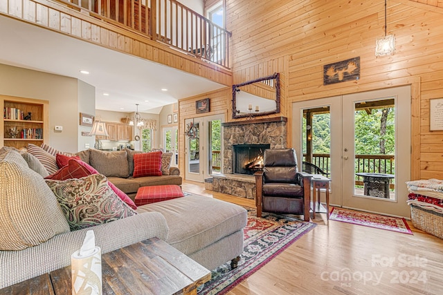 living room featuring wood walls, a fireplace, hardwood / wood-style floors, high vaulted ceiling, and a chandelier