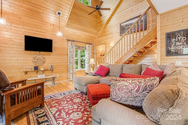 living room featuring high vaulted ceiling, hardwood / wood-style floors, ceiling fan, and wooden walls