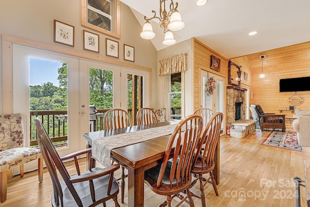 dining room with wooden walls, a fireplace, high vaulted ceiling, a chandelier, and light wood-type flooring