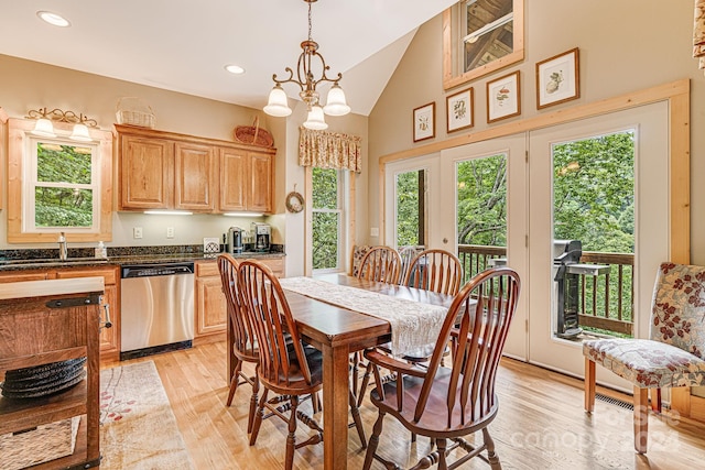 dining space with high vaulted ceiling, plenty of natural light, a chandelier, and light hardwood / wood-style flooring