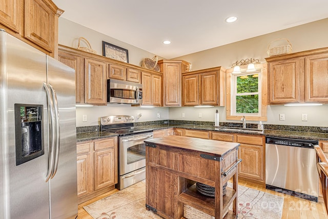 kitchen with dark stone counters, stainless steel appliances, sink, and light hardwood / wood-style floors