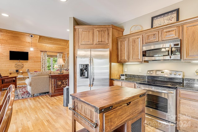 kitchen featuring light hardwood / wood-style flooring, stainless steel appliances, dark stone countertops, and wooden walls