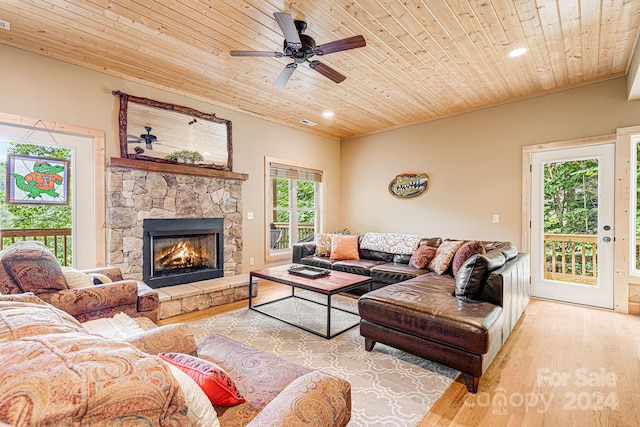 living room with light wood-type flooring, a stone fireplace, wood ceiling, and ceiling fan