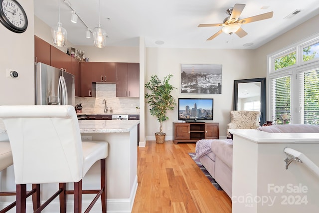 kitchen featuring decorative light fixtures, stainless steel refrigerator with ice dispenser, light hardwood / wood-style flooring, a breakfast bar, and decorative backsplash