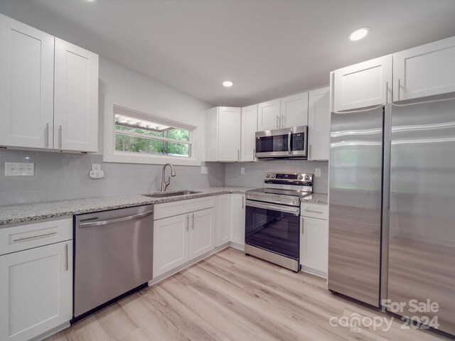 kitchen with light wood-type flooring, tasteful backsplash, appliances with stainless steel finishes, light stone counters, and sink