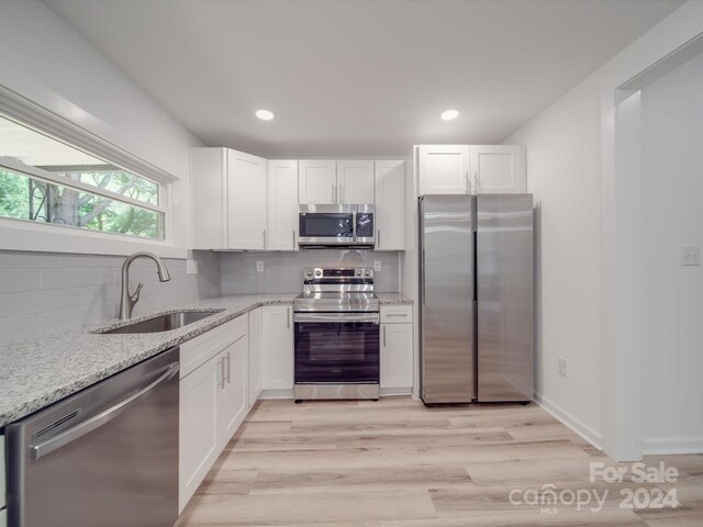 kitchen with light wood-type flooring, appliances with stainless steel finishes, sink, and backsplash