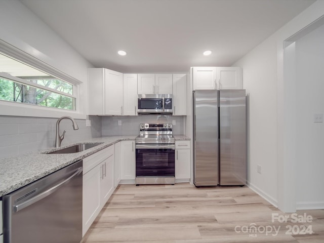 kitchen with stainless steel appliances, a sink, light stone countertops, and white cabinets