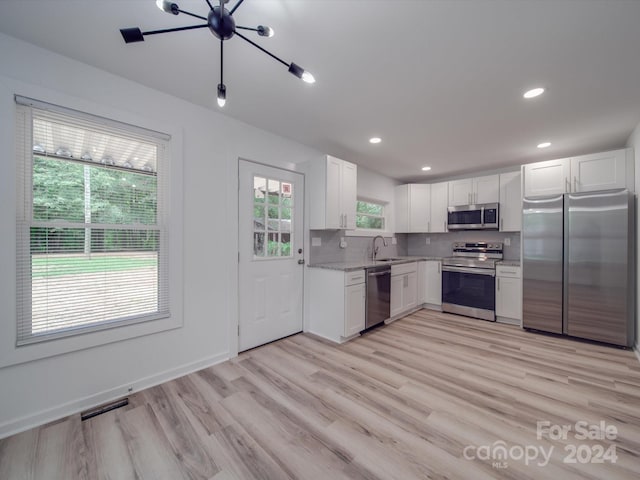 kitchen with backsplash, sink, light wood-type flooring, stainless steel appliances, and white cabinets