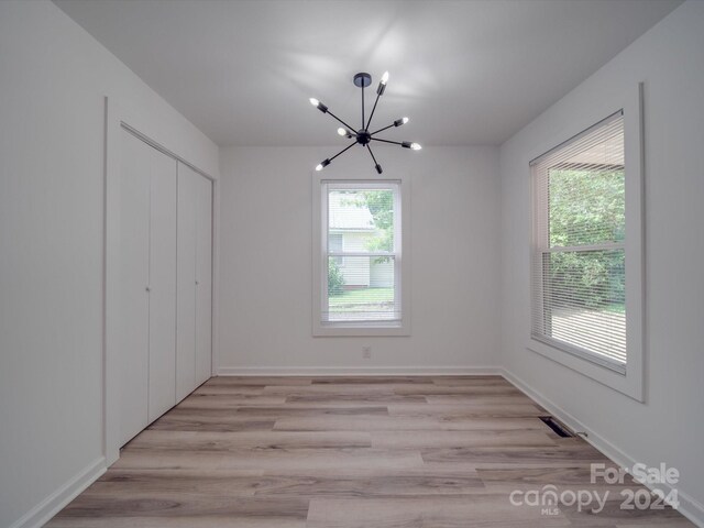 unfurnished bedroom with light hardwood / wood-style floors, a notable chandelier, and a closet