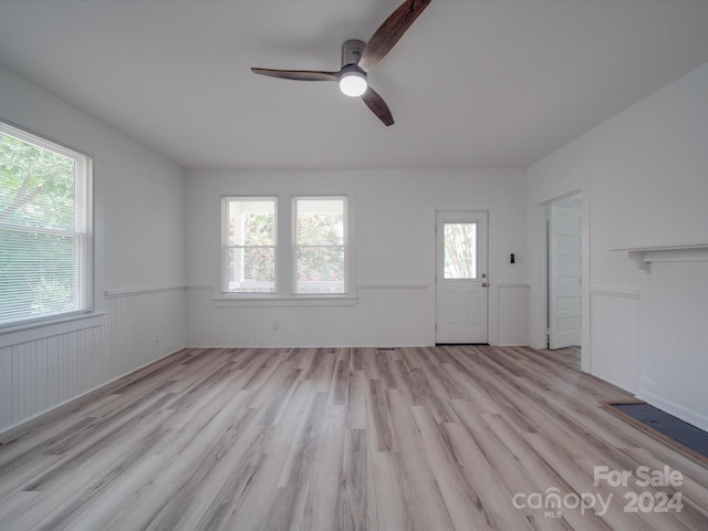 unfurnished living room with light wood-type flooring, ceiling fan, and wainscoting