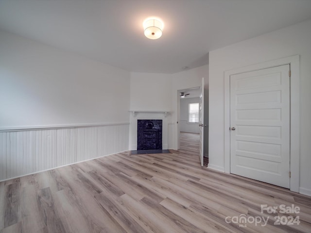 unfurnished living room with a wainscoted wall, a fireplace with flush hearth, and wood finished floors