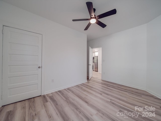 empty room with baseboards, a ceiling fan, and light wood-style floors